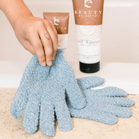 Heavy exfoliating gloves with a bottle of 'Beauty by Earth' self tanner in the background.