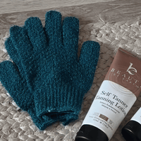 Medium exfoliating gloves and a tube of self tanning lotion on a textured surface