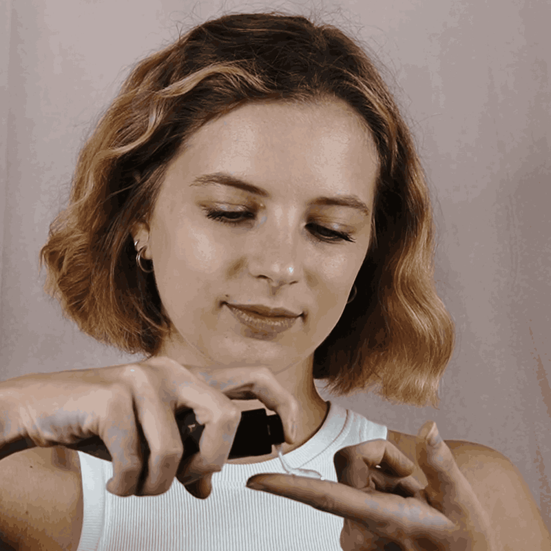 Woman holding a small object close to her face against a neutral background