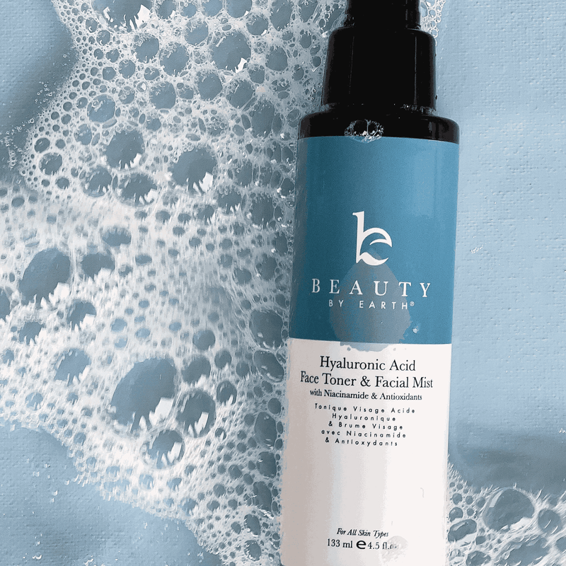 Beauty by Earth Hyaluronic Acid Face Toner & Facial Mist bottle with a blue and white label on a textured blue background.
