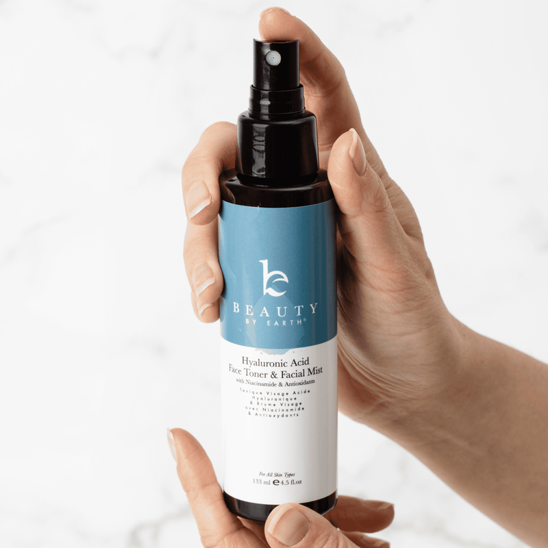 Hand holding a bottle of 'Beauty by Earth' facial mist against a white background
