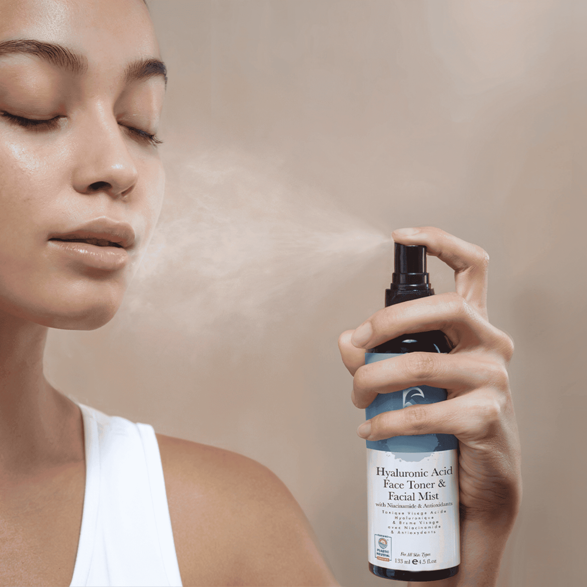 Person using a bottle of facial mist with a neutral background