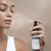Person using a bottle of facial mist with a neutral background