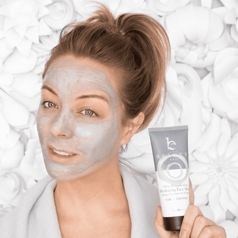 Woman applying a face mask with a tube of the same product in front of her.