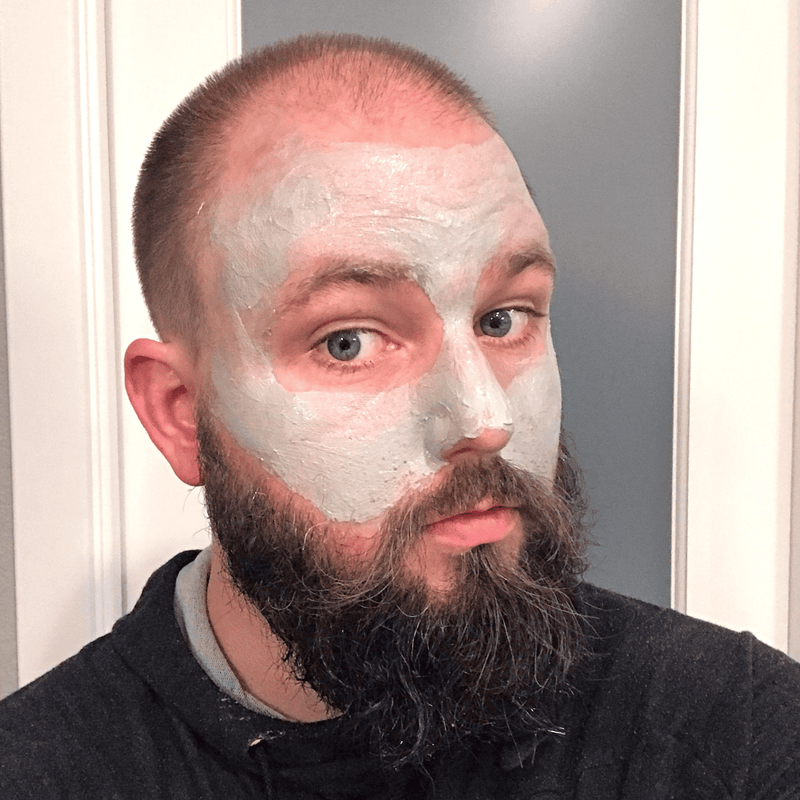 Man with a beard wearing a white face mask indoors.