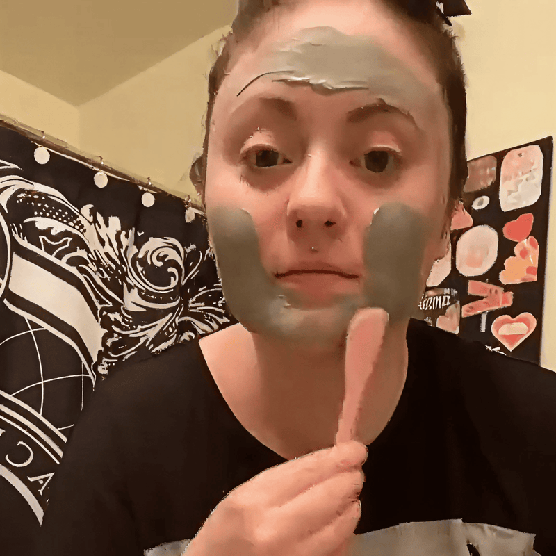 Person applying a face mask with a spatula in front of a decorated wall.