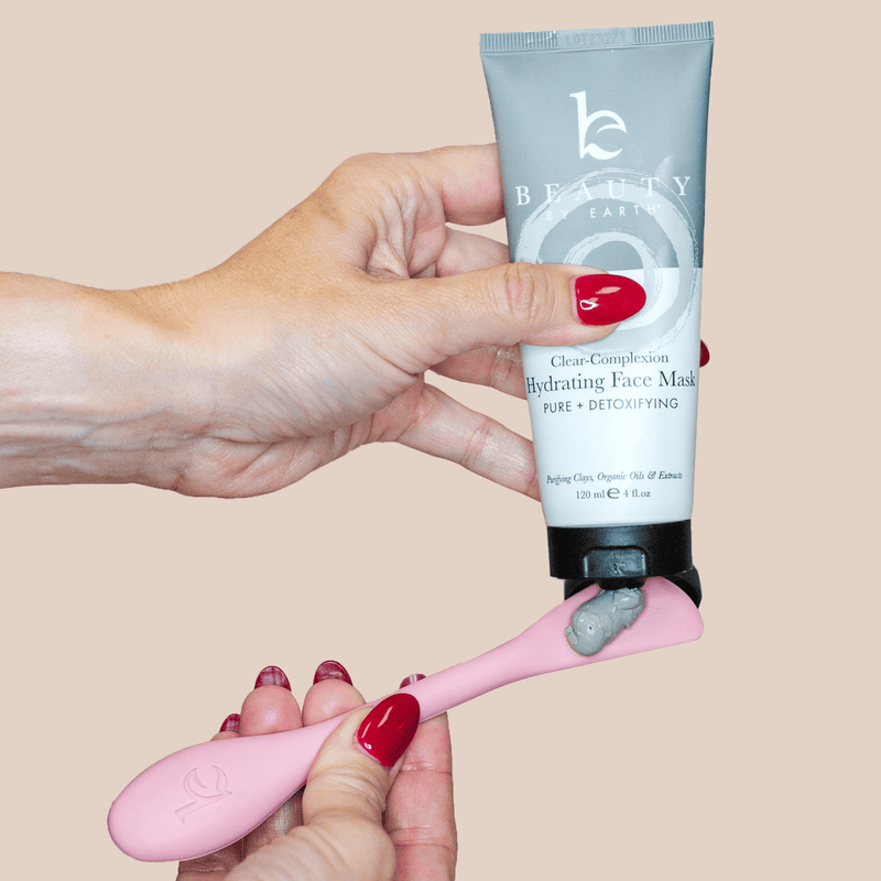 Hand holding a pink face mask applicator with a tube of Beauty Earth face mask on a beige background