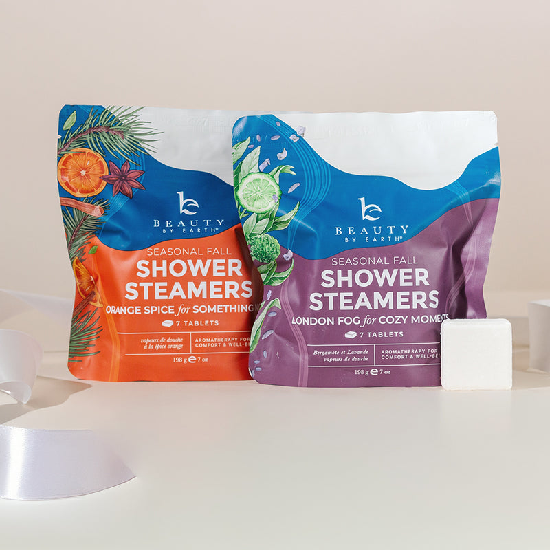 Two packages of Beauty by Earth shower steamers on a white surface with a beige background.