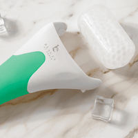 White and green skincare ice roller tool on a marble surface