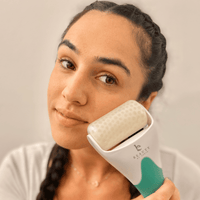 Woman using a skincare tool ice roller on her face with a neutral background