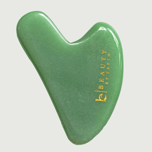 Green jade gua sha tool with 'Beauty by Earth' branding on a light gray background