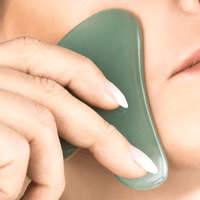 Person using a green gua sha tool on their skin
