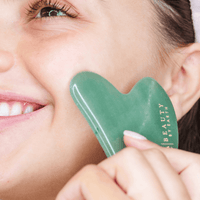 Woman using a green jade gua sha tool on her face with a close-up view.