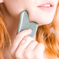 Person using a gua sha tool on their neck with a blurred background