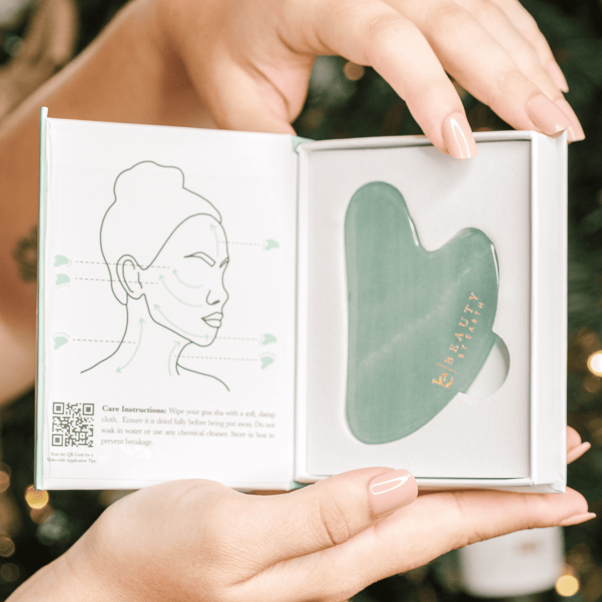 Green facial gua sha iin a box held by hands with a blurred background