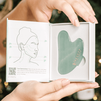 Green facial gua sha iin a box held by hands with a blurred background