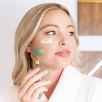 Woman using a jade roller on her face with a neutral background