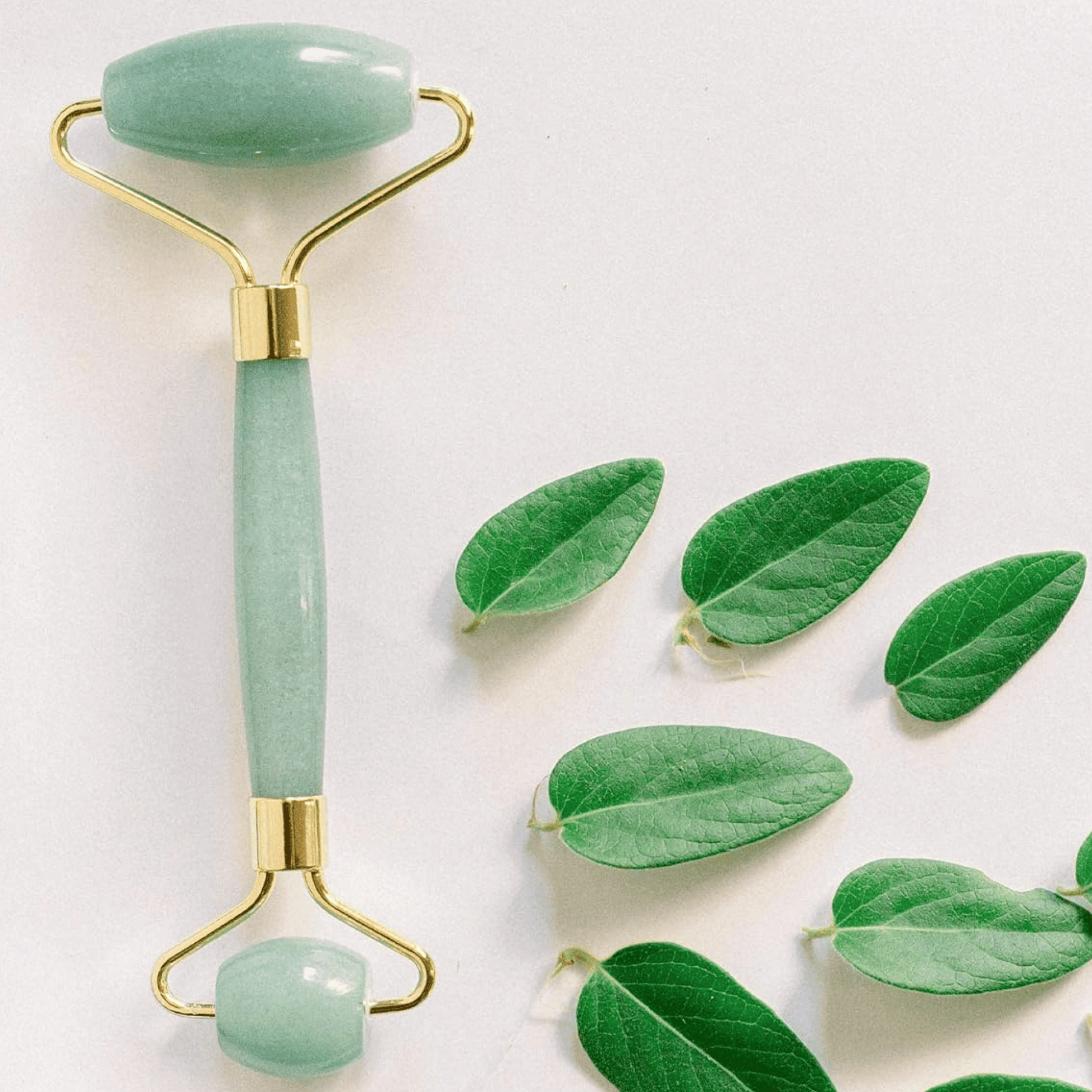Green jade roller with gold accents on a white background with green leaves.
