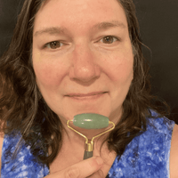 Woman holding a jade roller against her face with a dark background