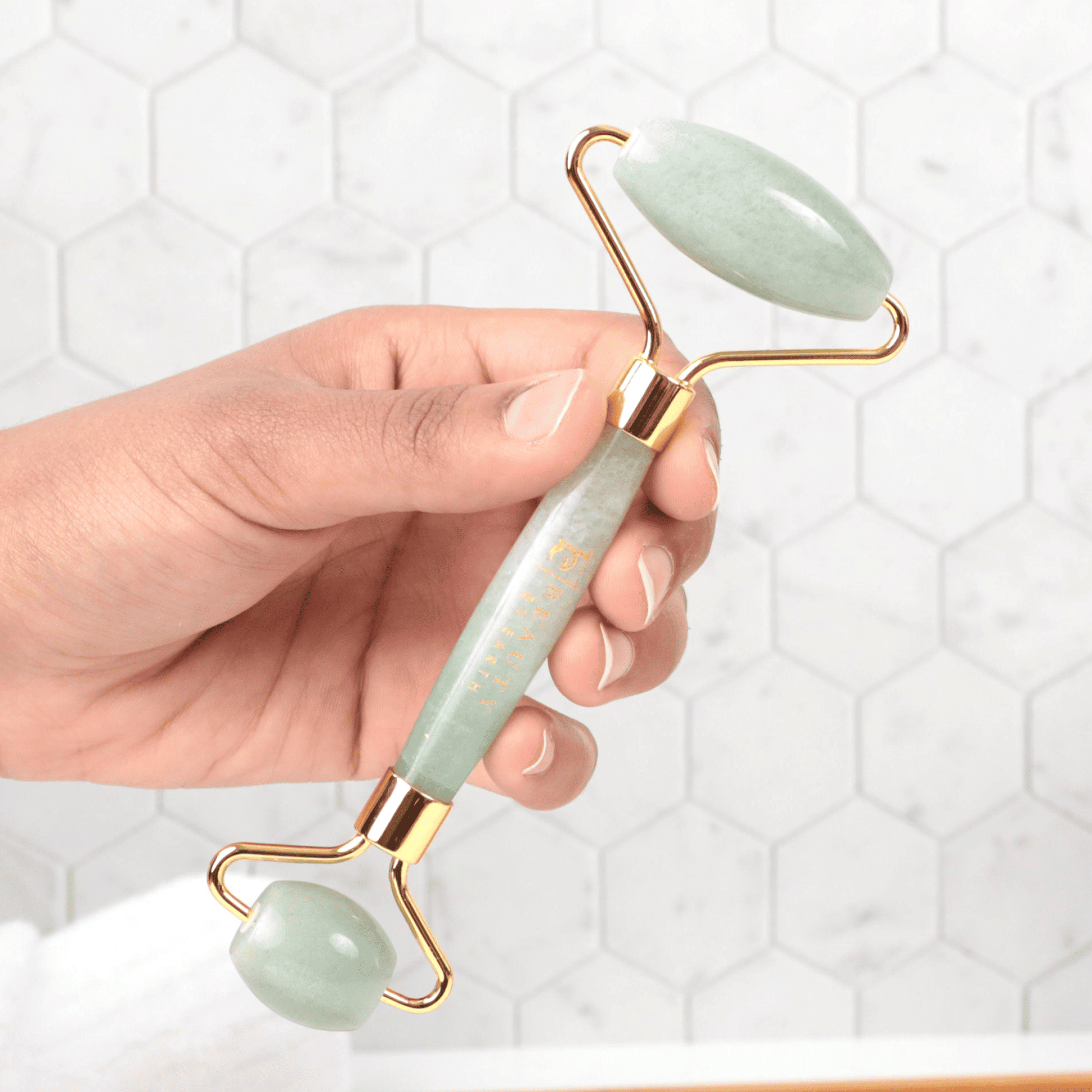 Hand holding a jade roller with gold accents against a white background