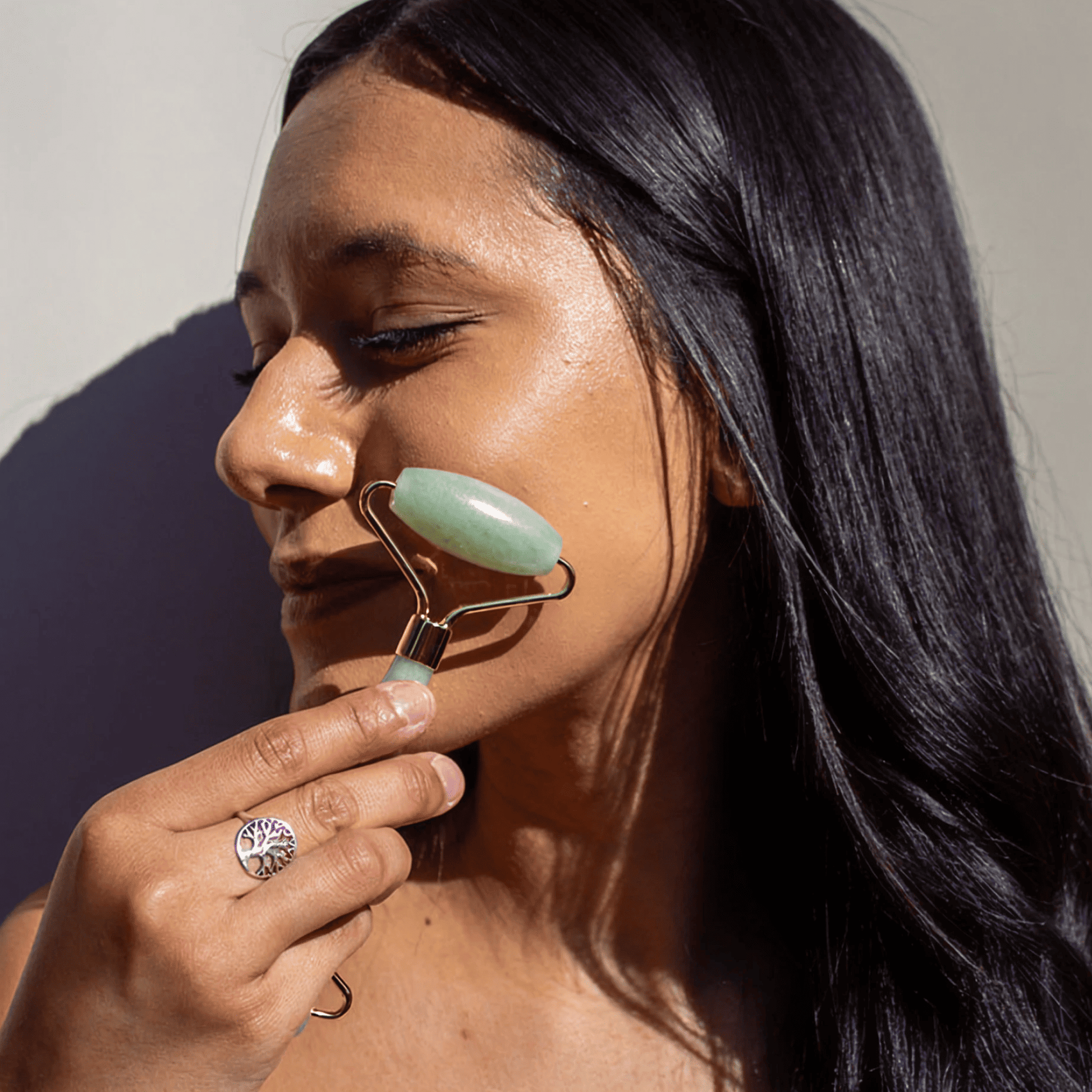 Woman using a jade roller on her face with a neutral background