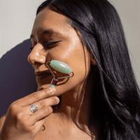 Woman using a jade roller on her face with a neutral background