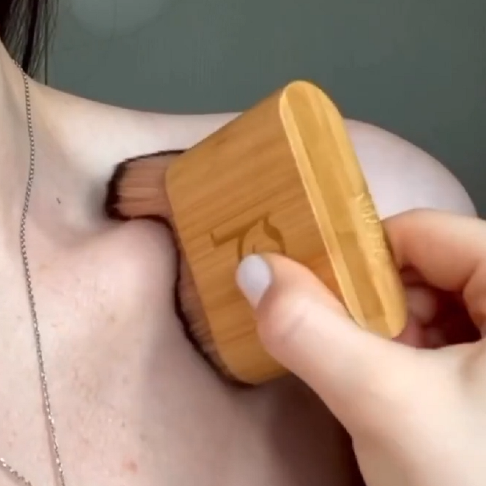 Person using a wooden brush on their shoulder against a neutral background