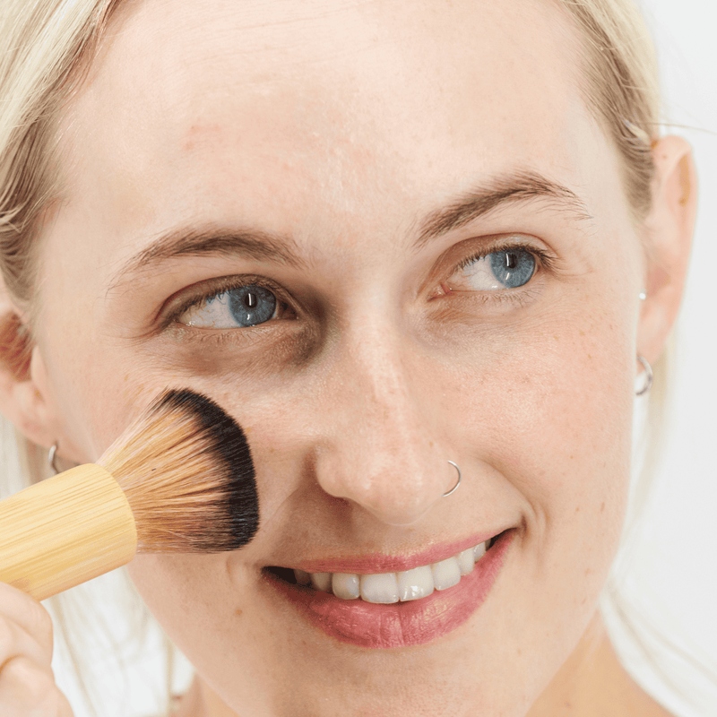 Woman applying makeup with a brush on a neutral background