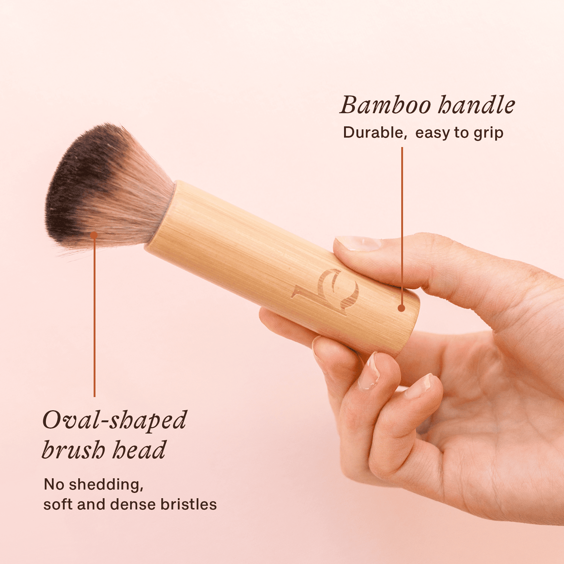 Makeup brush with bamboo handle and oval-shaped brush head, held by a hand on a pink background.