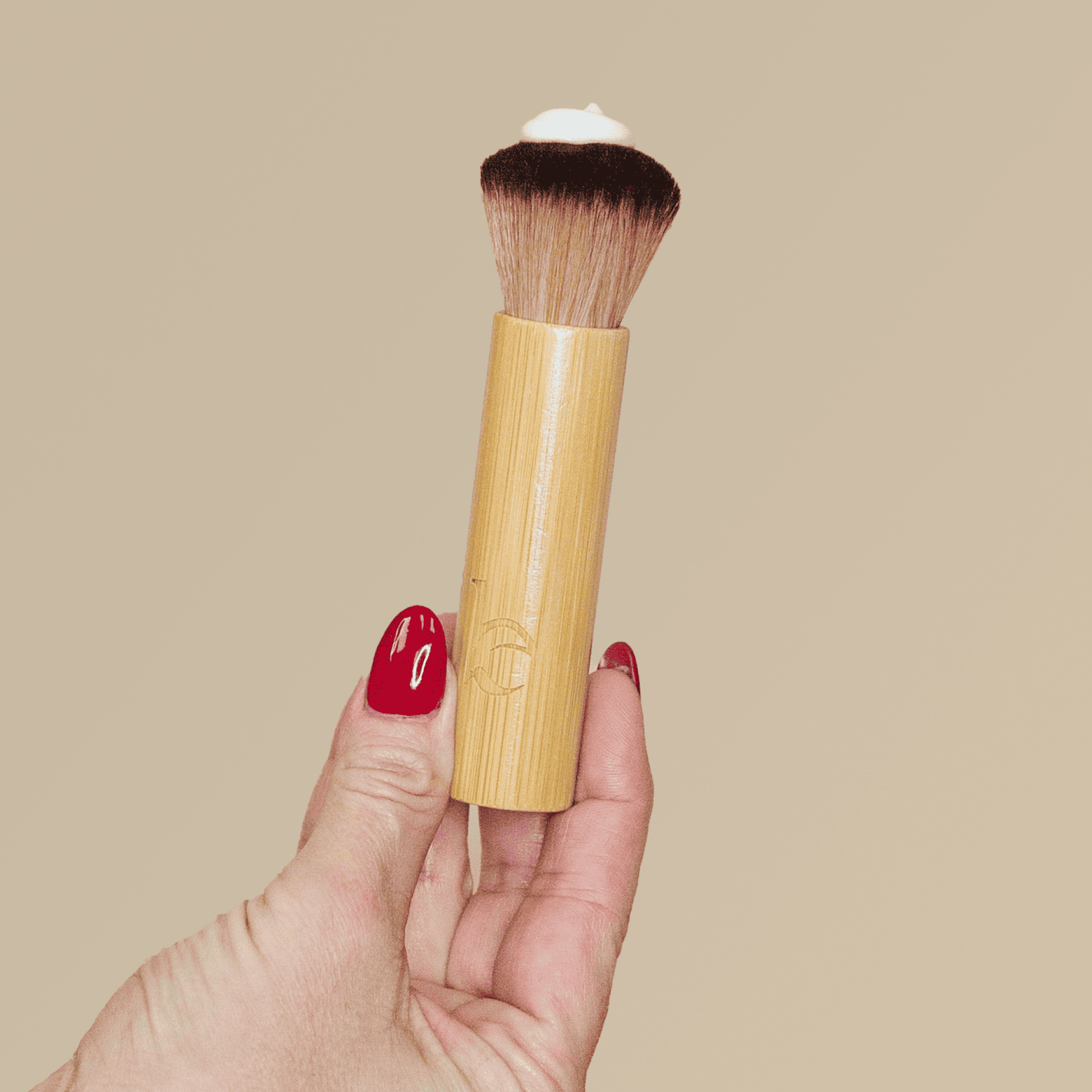 Makeup brush with bamboo handle held by a hand against a beige background