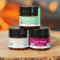 Three jars of lip scrub with different flavors on a wooden surface.