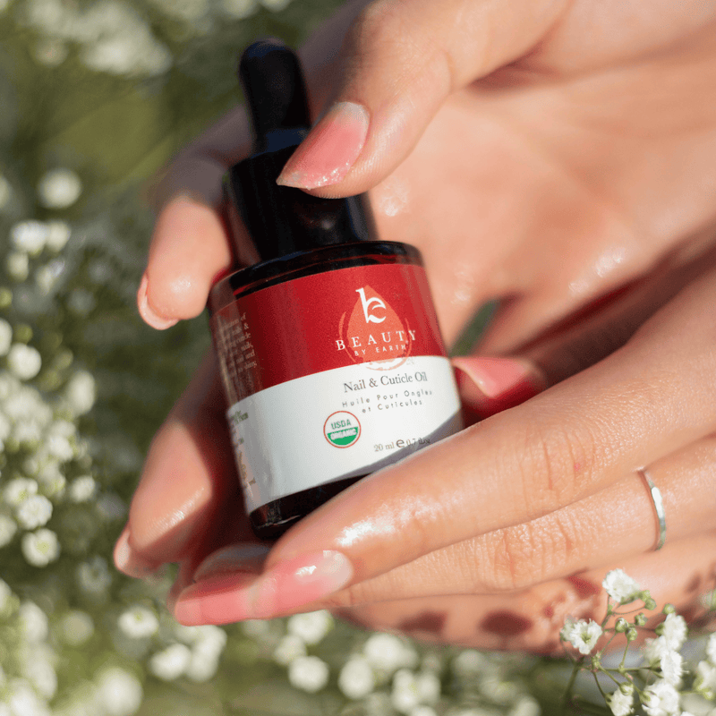 Hand holding a bottle of Beauty by Earth nail and cuticle oil with a natural background