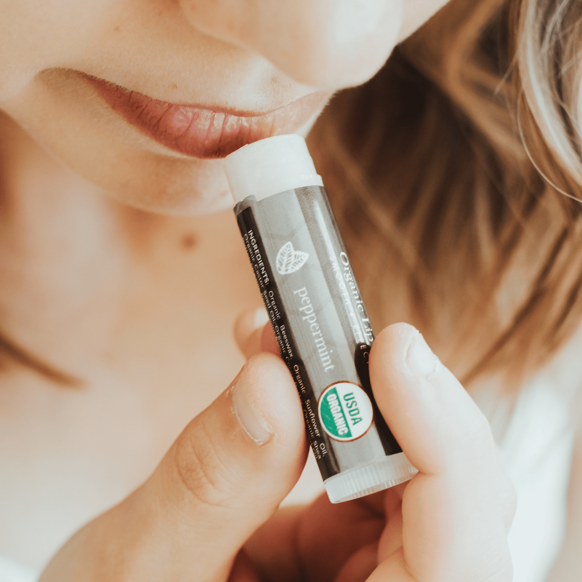 Person holding a lip balm tube labeled 'peppermint' with a blurred background