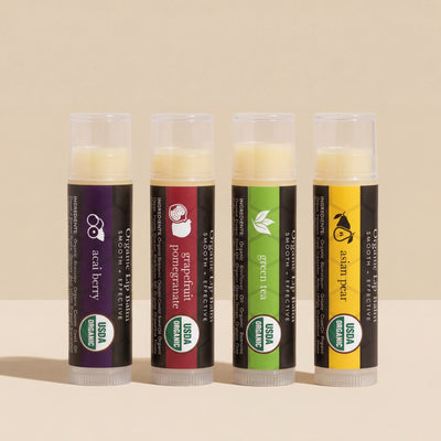 Four organic lip balm tubes with different flavors on a beige background