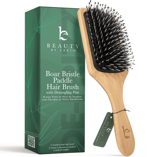 Wooden paddle hair brush with black bristles next to its packaging on a white background