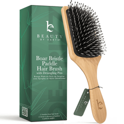 Wooden paddle hair brush with black bristles next to its packaging on a white background