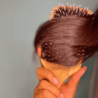 Person using a hairbrush with pins to style hair against a neutral background