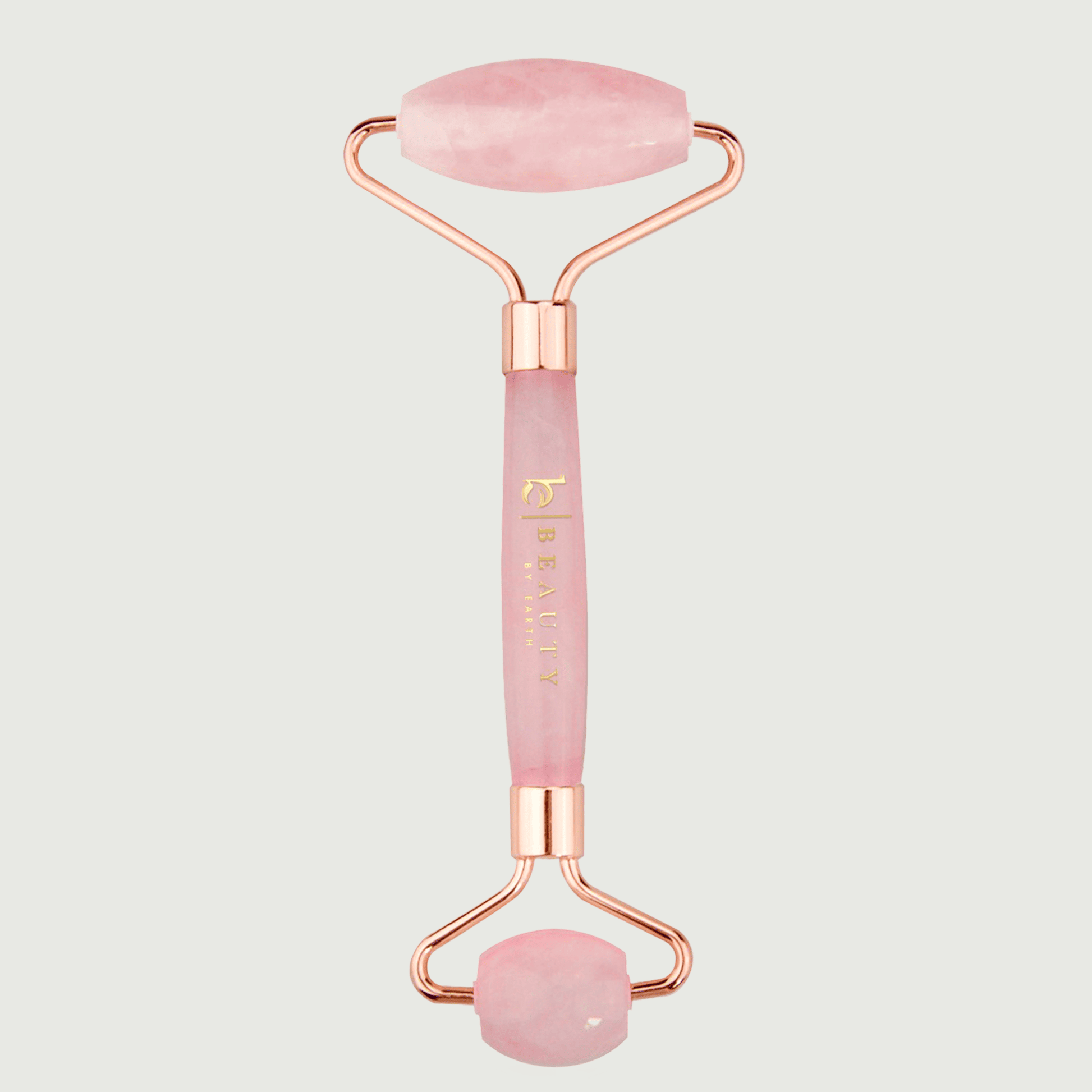 Pink and rose gold facial roller on a light gray background
