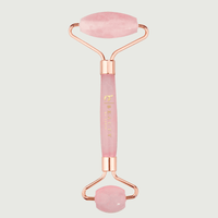 Pink and rose gold facial roller on a light gray background