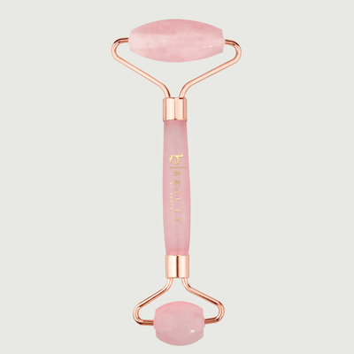 Pink and rose gold facial roller on a light gray background