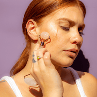 Woman wearing a pink crystal earring against a purple background