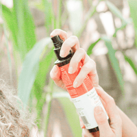 Person holding a red spray bottle with a black nozzle against a blurred green background