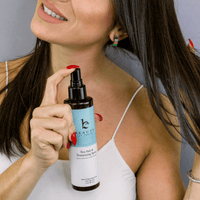 Woman holding a bottle of 'beauty' sea salt spray against a neutral background
