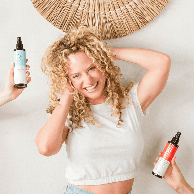 Woman with curly hair holding a bottle of hair product against a neutral background