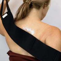 Person wearing a black strap across their shoulder with a white substance on the skin.