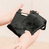 Black face mask held in a hand against a beige background