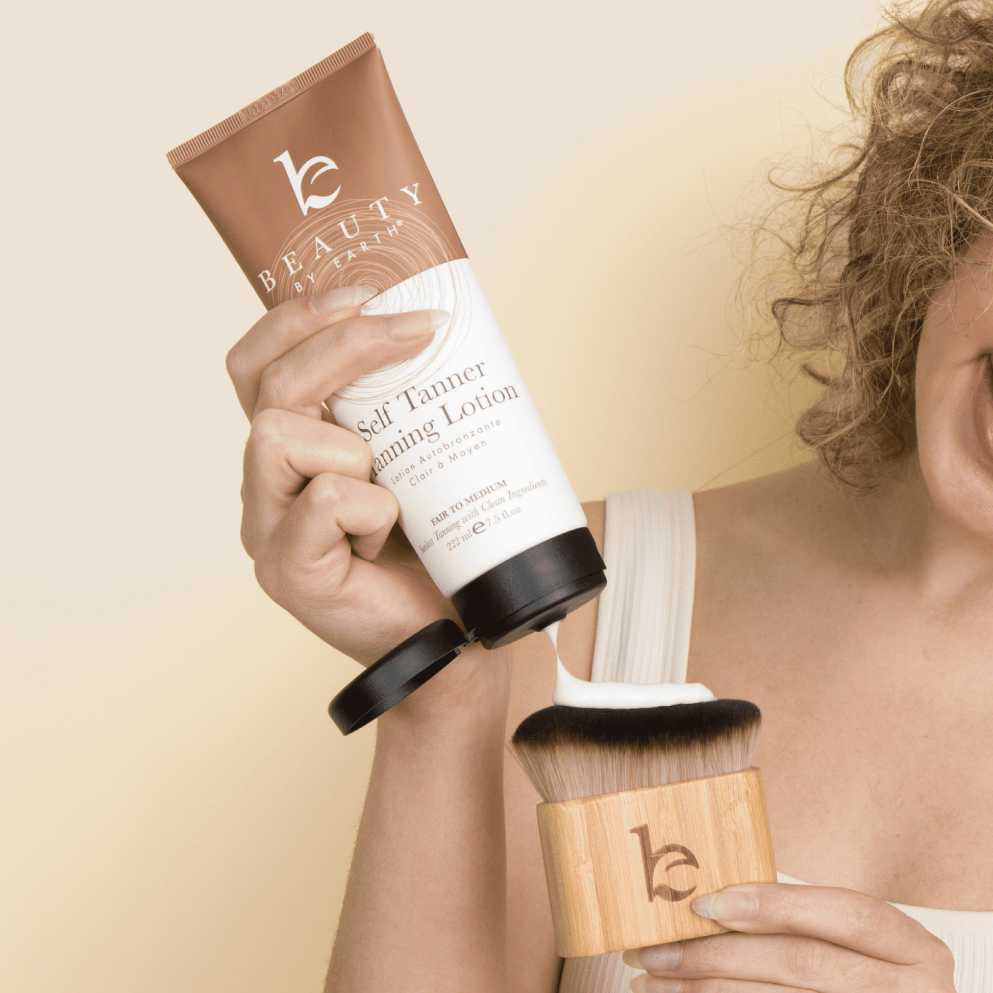 Model holding self tanning body lotion in one hand and squeezing the white lotion onto the kabuki body blending brush in the other hand. 