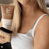 Person holding a 'Beauty by Earth' self tanner body lotion and kabuki body blending brush