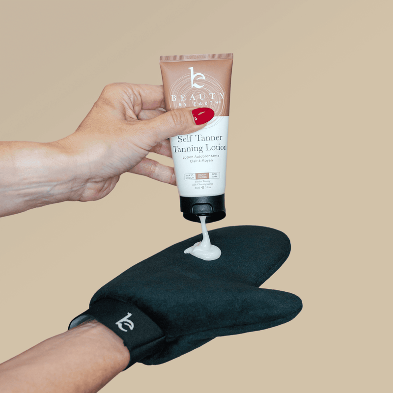 Hand applying tanning lotion to a black glove on a beige background