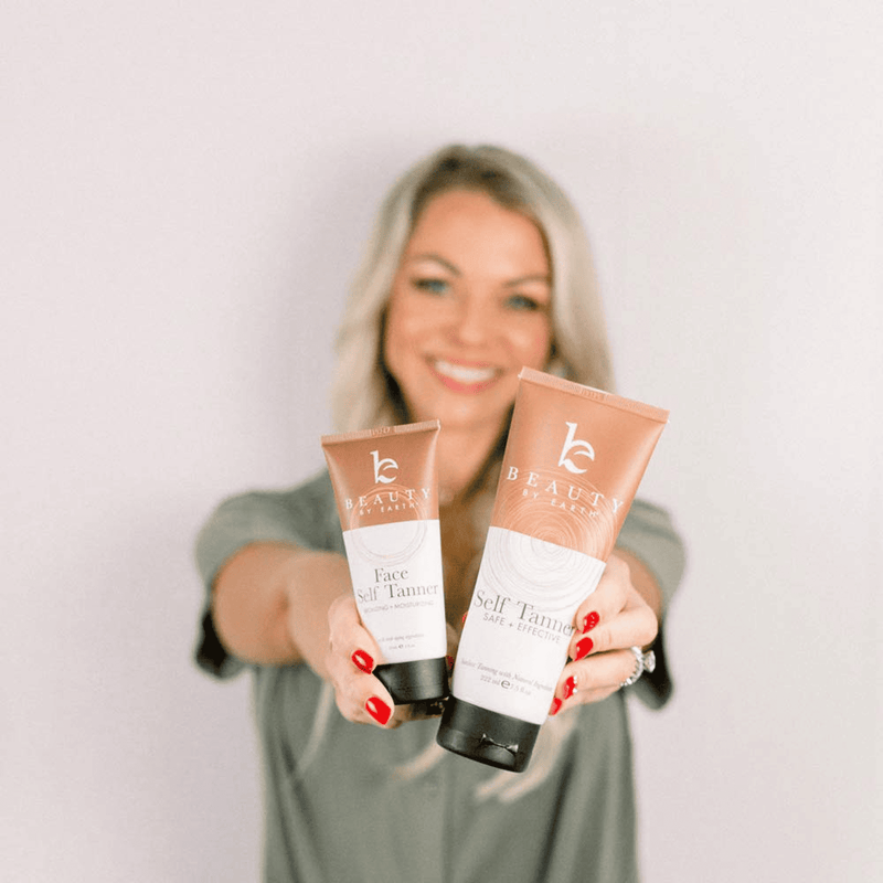 A model holding bottles of self tanning body and face lotions in hands focused, the model is blurred in the background.